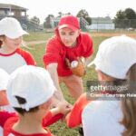 Little league baseball team put hands in middle of huddle with coach during game